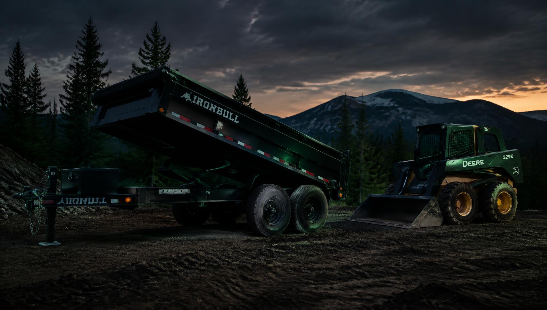 Dump trailer and skid steer at a job site at dusk